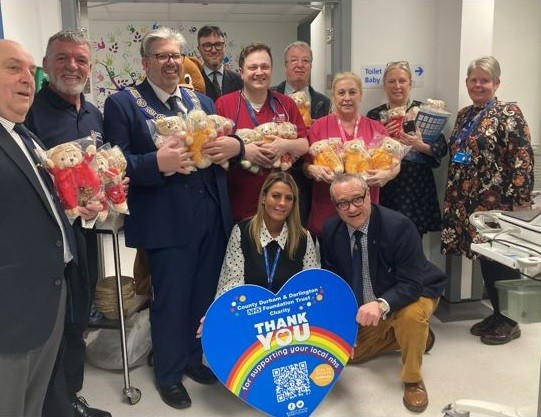 People smiling holding teddy bears and a large heart inside the children's emergency department