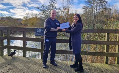 man and woman holding certificate on a bridge outside with water and sky behind them