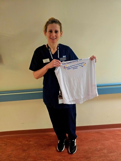 Woman in blue scrubs holding up a white charity tshirt